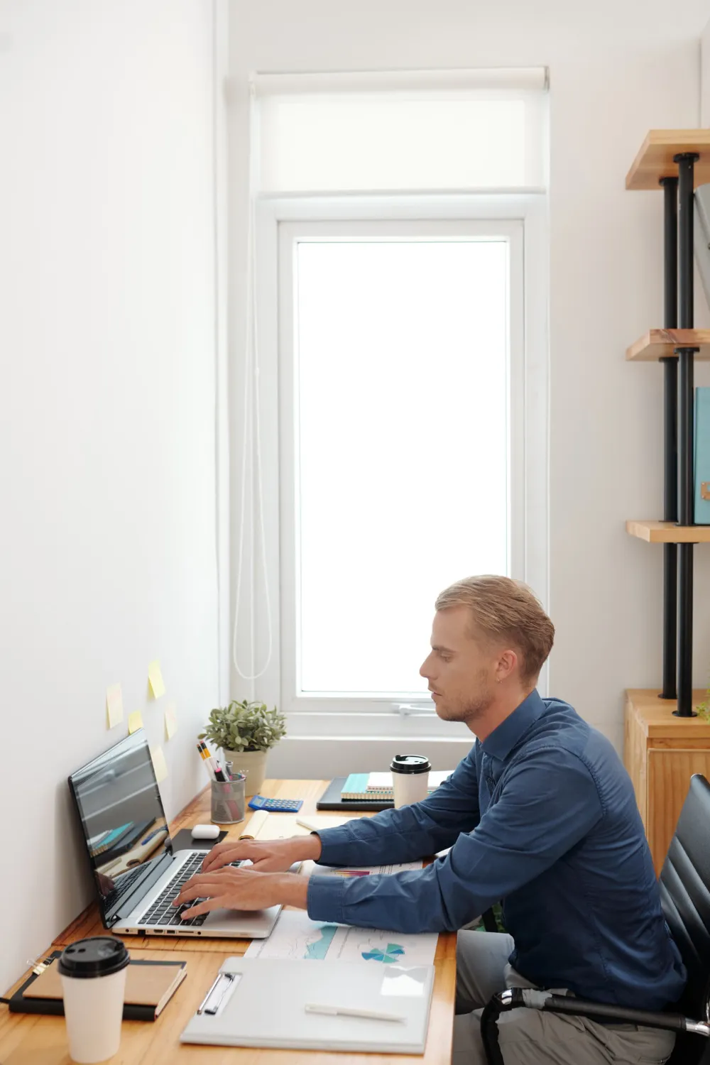 young-businessman-working-laptop-office-table-analyzing-financial-charts-filling-report-document